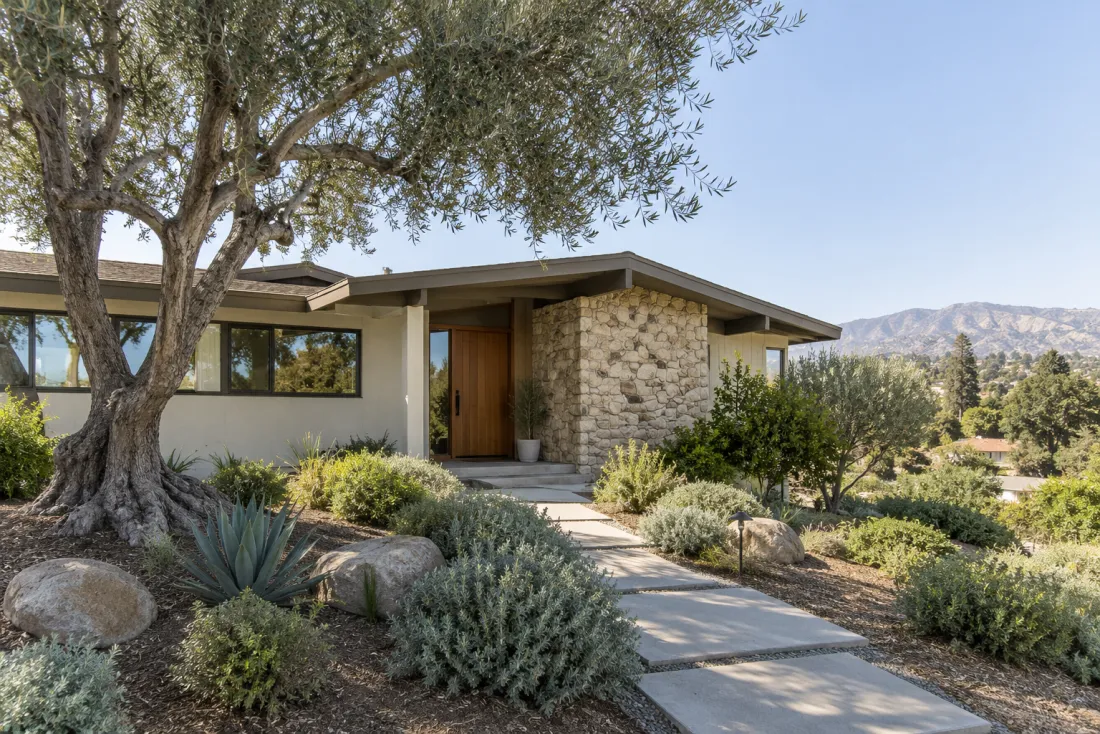 Representative neighborhood scene: A hillside ranch home with a stone entry wall and native planting